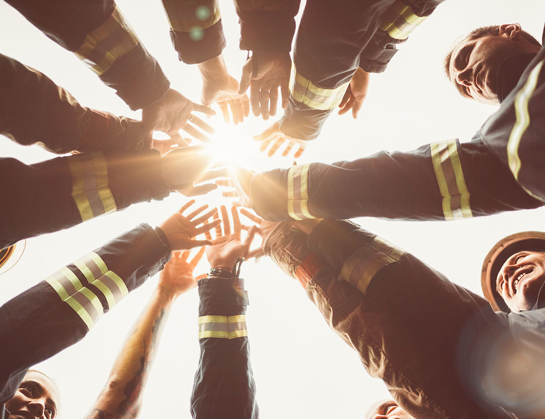 Feuerwehrmänner welche ihre Hände übereinander gelegt haben um den Teamgeist zu stärken.